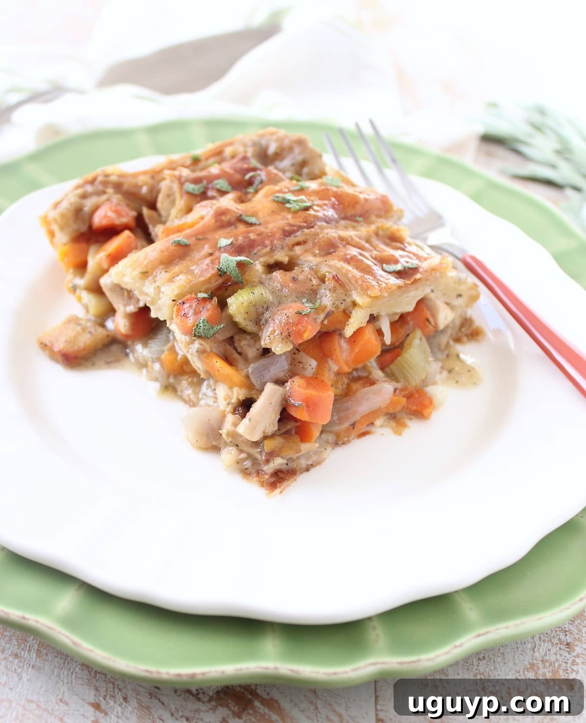 A generous slice of Turkey Pot Pie with a golden, flaky puff pastry crust, revealing the rich, creamy filling of turkey and mixed vegetables, served on a white plate.