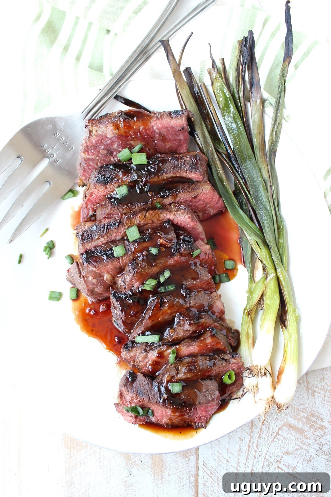 Close-up of cooked, thinly sliced boneless short ribs on a plate, glistening with Korean BBQ sauce and garnished with grilled green onions.