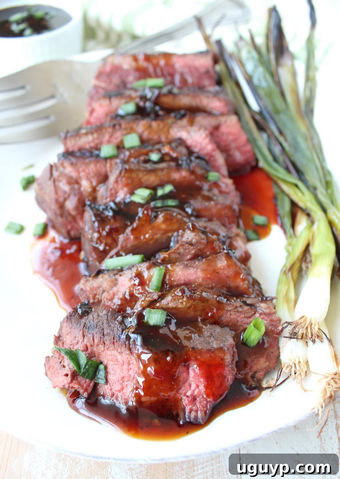 Artfully arranged sliced cooked short ribs on a plate, generously coated in Korean BBQ sauce and topped with diced green onions. Grilled green onions accompany the dish.