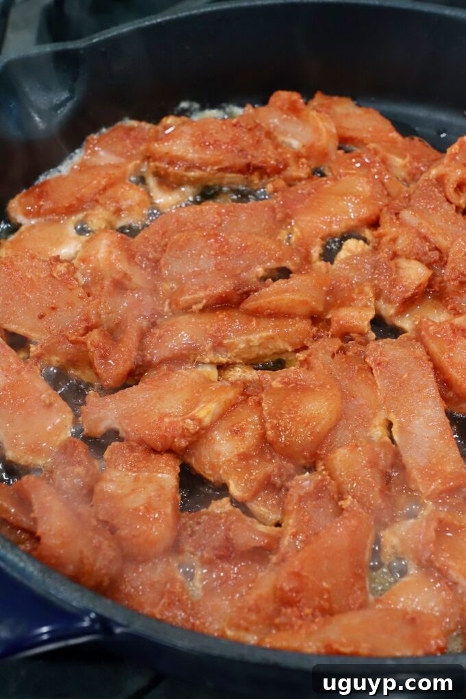 sliced raw chicken coated in spices, cooking in cast iron skillet