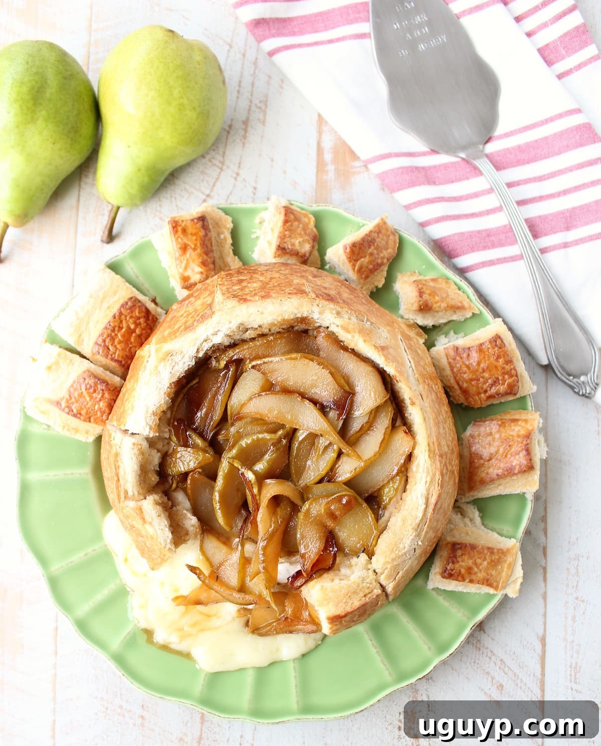 A beautifully baked brie bread bowl, with golden-brown crust and a hint of melted cheese peeking through, topped with caramelized Bartlett pears.