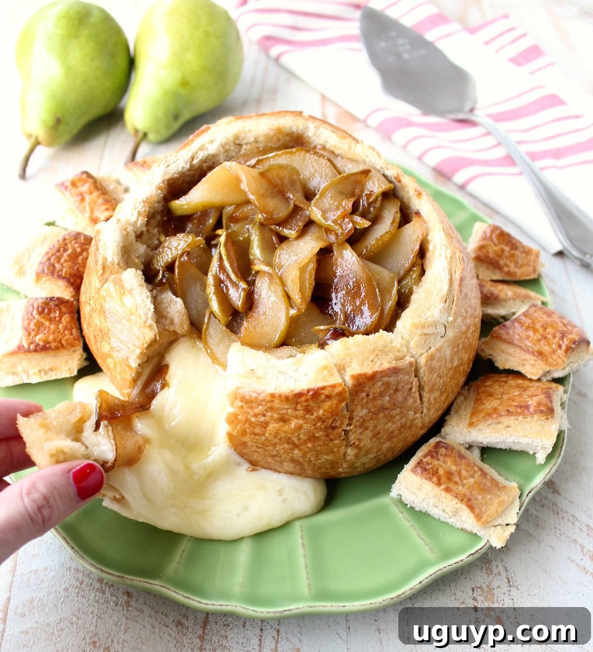 A stunning Caramelized Pear Baked Brie Bread Bowl, presented with fresh pear slices and toasted sourdough bread pieces for dipping, inviting guests to indulge.