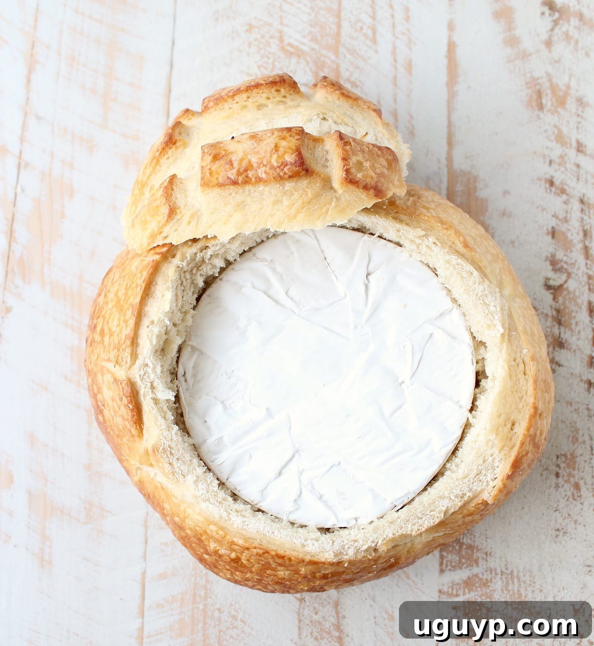 A sourdough bread bowl with a round of brie cheese perfectly nestled in its hollowed center, ready for toppings.