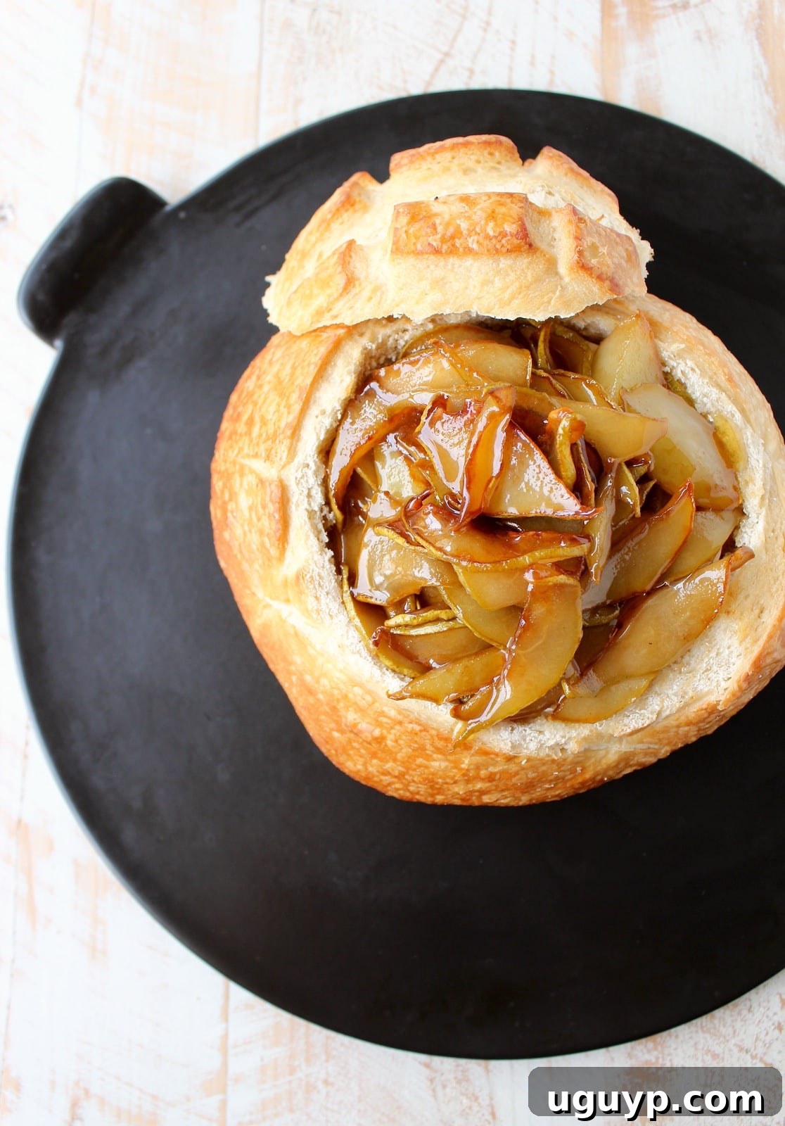 A sourdough bread bowl on a baking sheet, now filled with brie, topped with glistening caramelized pears and honey, ready for baking.