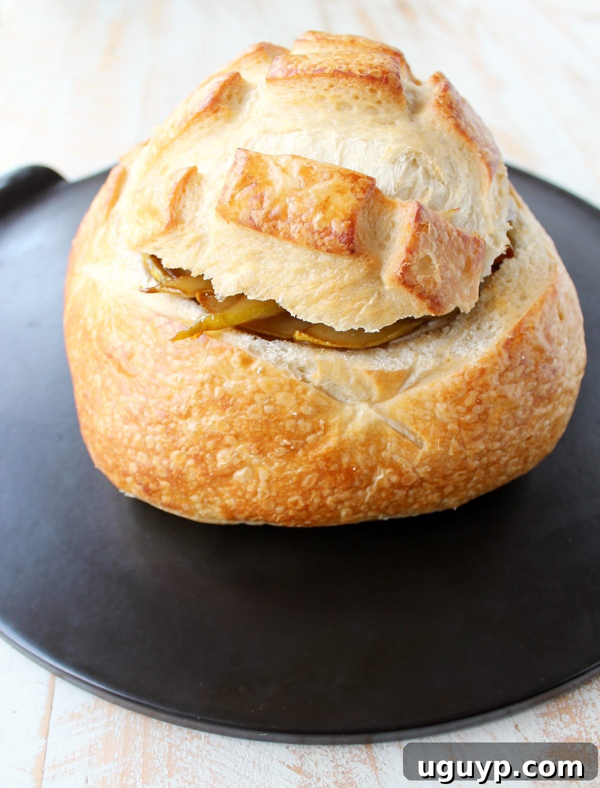 The fully assembled sourdough bread bowl, filled with brie and caramelized pears and covered with its top slice, resting on a baking sheet before going into the oven.