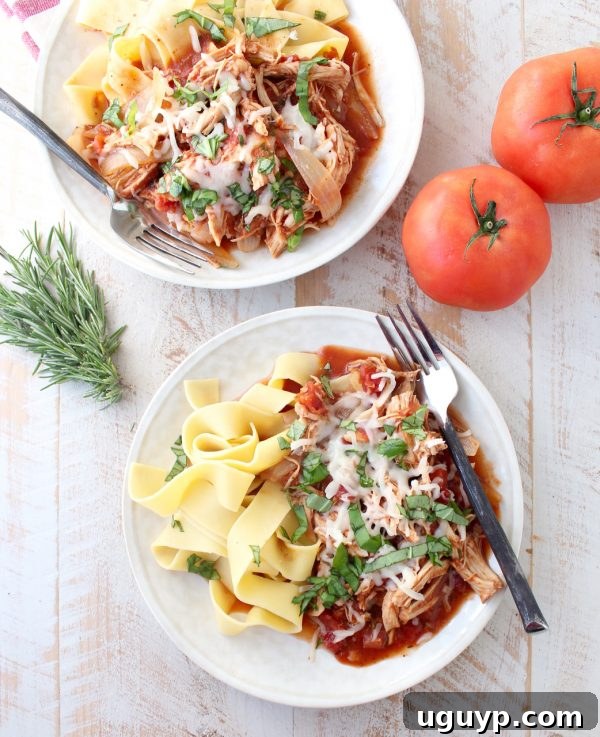 Two white plates featuring slow cooker chicken ragu over pasta, garnished with melted cheese and fresh herbs, arranged on a rustic wooden surface for a cozy dinner setting.