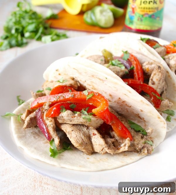 A beautifully arranged serving of Jerk Chicken Fajitas, with chicken, peppers, and onions overflowing from warm tortillas, garnished with fresh cilantro and lime wedges.