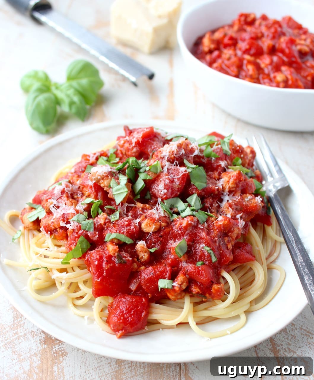 A plate of Roasted Red Pepper Turkey Bolognese served over traditional spaghetti noodles, with a fork ready to enjoy, garnished with a sprig of fresh basil.