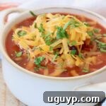 Rich chicken enchilada soup in a white crock, generously topped with melted cheddar cheese.