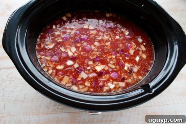 All the delicious ingredients for the chicken enchilada soup, including diced tomatoes with green chiles, sriracha, and beans, are combined in the slow cooker.