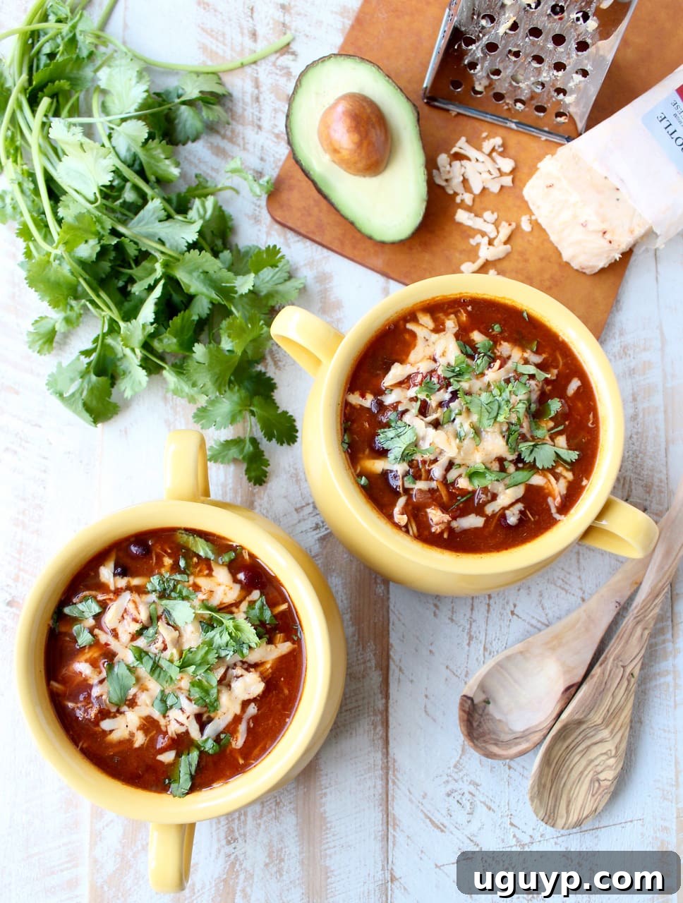 Two cheerful yellow bowls on a rustic wooden surface, brimming with savory enchilada soup, each adorned with a generous topping of shredded cheese and fresh cilantro.