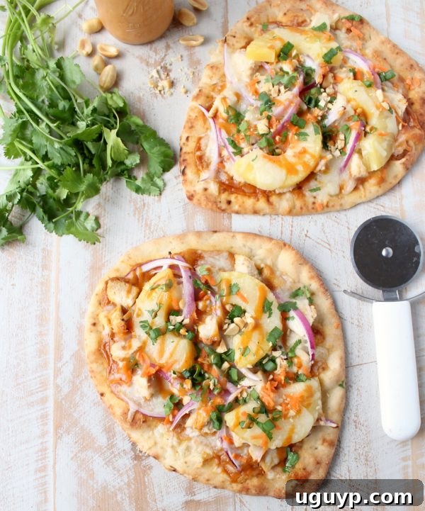 Ingredients being assembled on a naan bread base for Thai Peanut Chicken Pizza, including peanut sauce, grilled chicken, red onion, and pineapple.