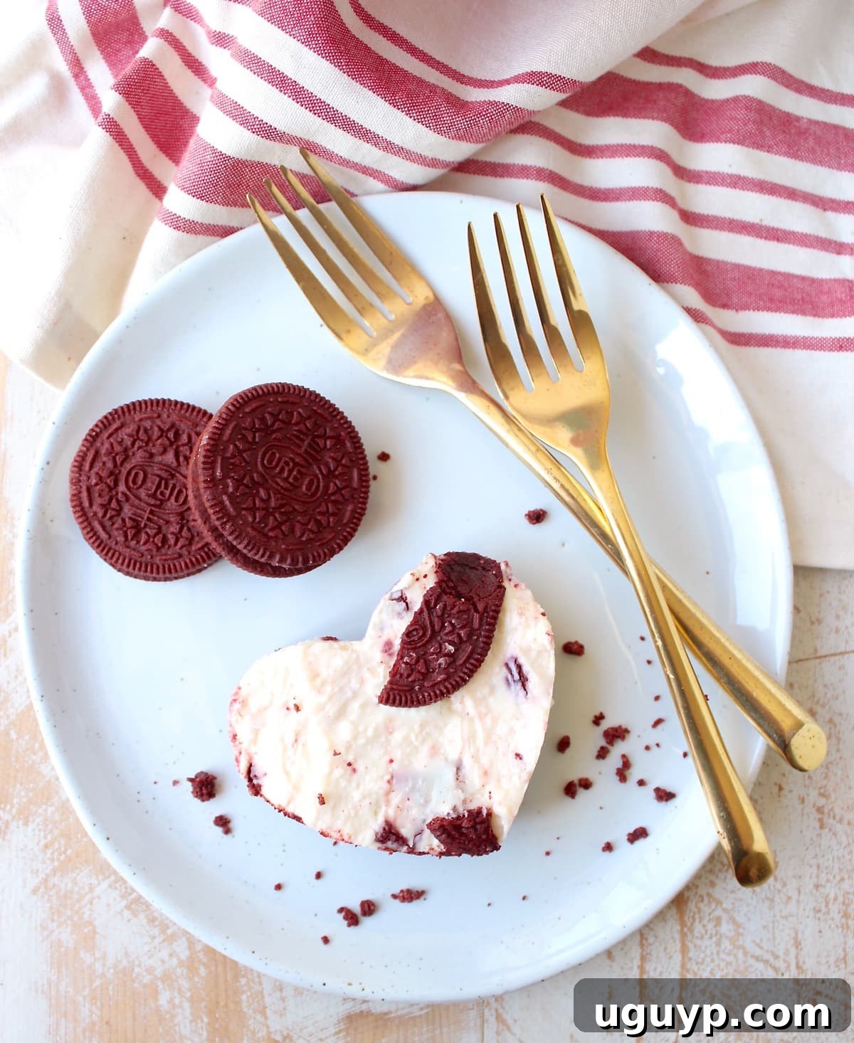 Heart-shaped Red Velvet Oreo cheesecake bar on a white plate with gold forks, showcasing a festive Valentine's Day dessert.