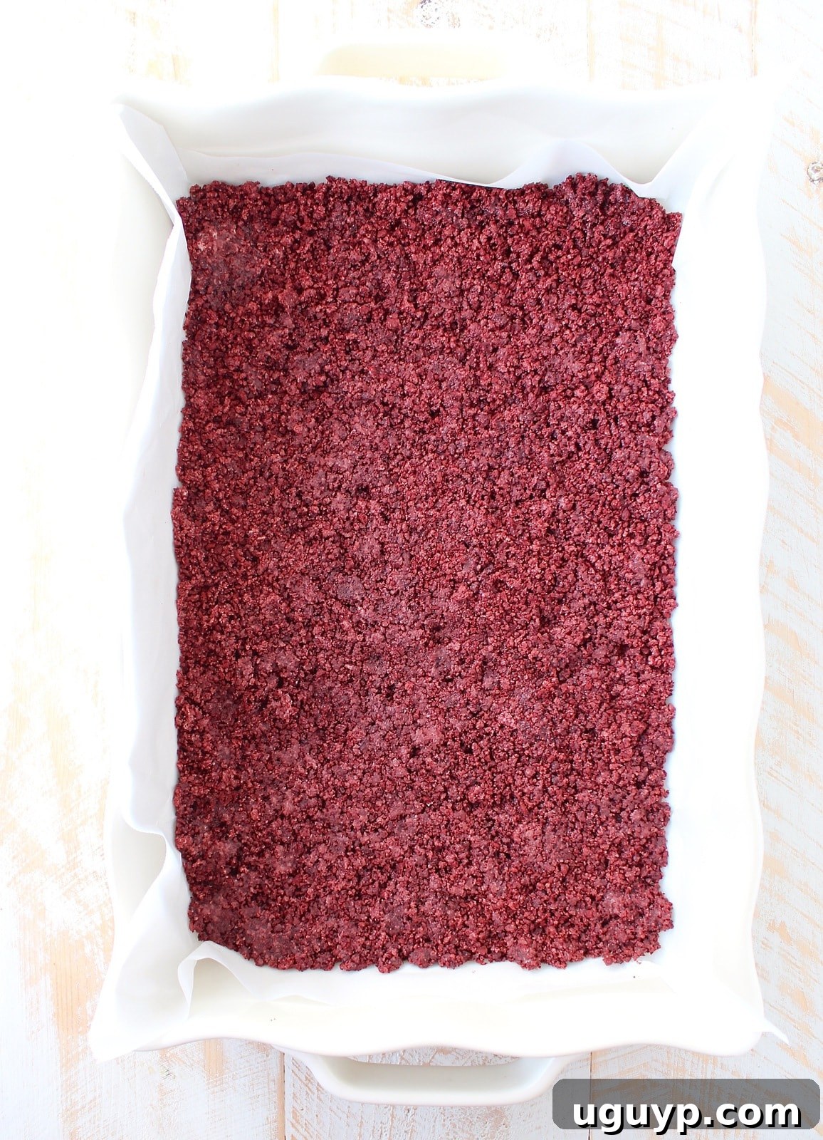 Crushed Red Velvet Oreos mixed with butter, pressed firmly into a parchment-lined baking dish to form the cheesecake crust.