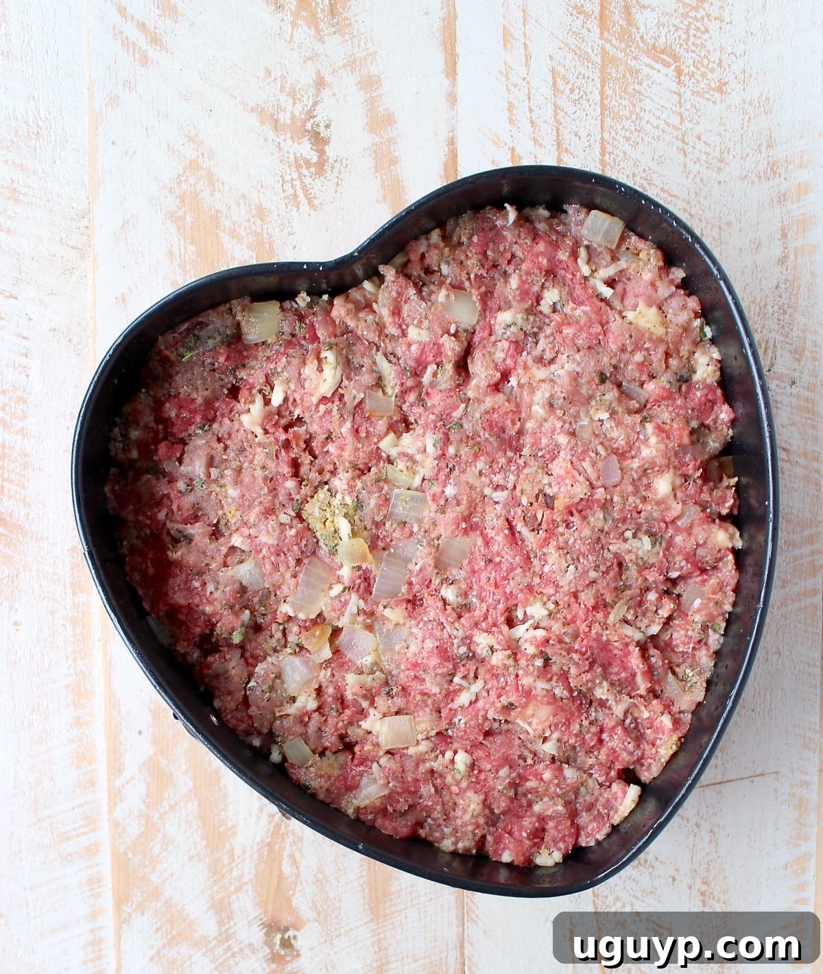 Italian Meatloaf mixture being pressed into a heart-shaped pan, ready for baking.