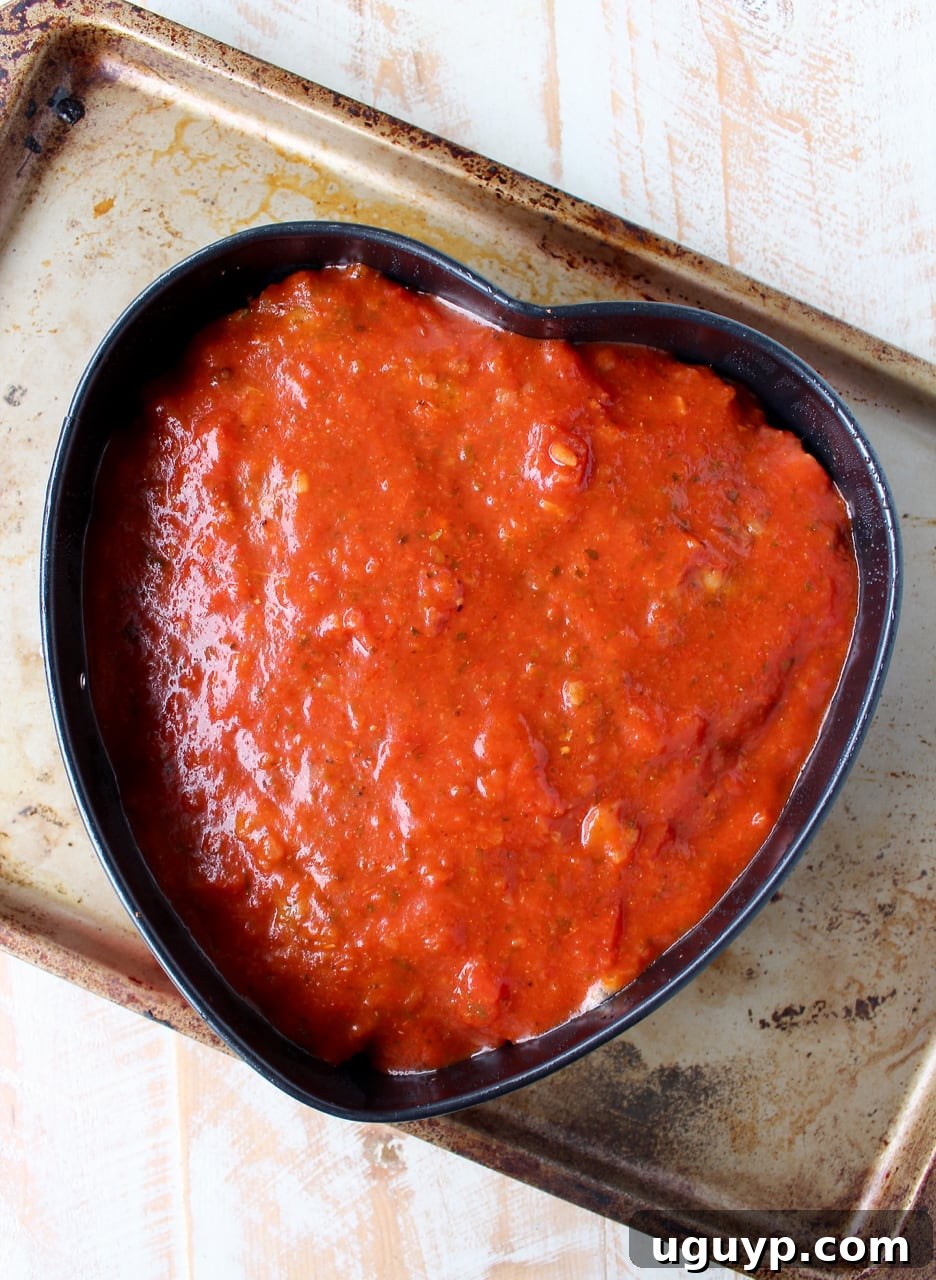 Applying a generous layer of marinara sauce over the partially baked Italian Meatloaf for a rich, flavorful glaze.