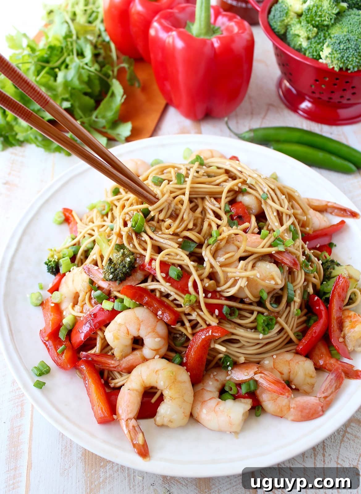 cooked shrimp, vegetables and noodles on a plate with chopsticks twirling the noodles