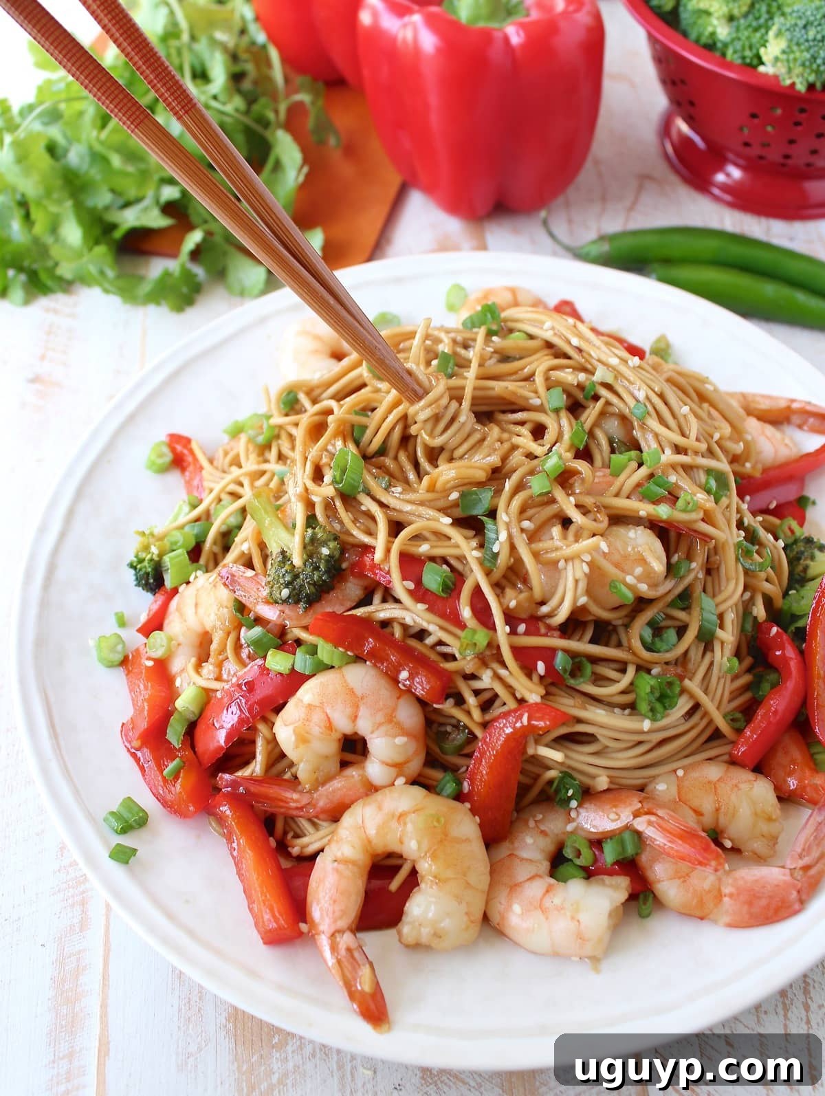 noodles tossed with shrimp, vegetables and teriyaki sauce on a plate with chopsticks in the noodles