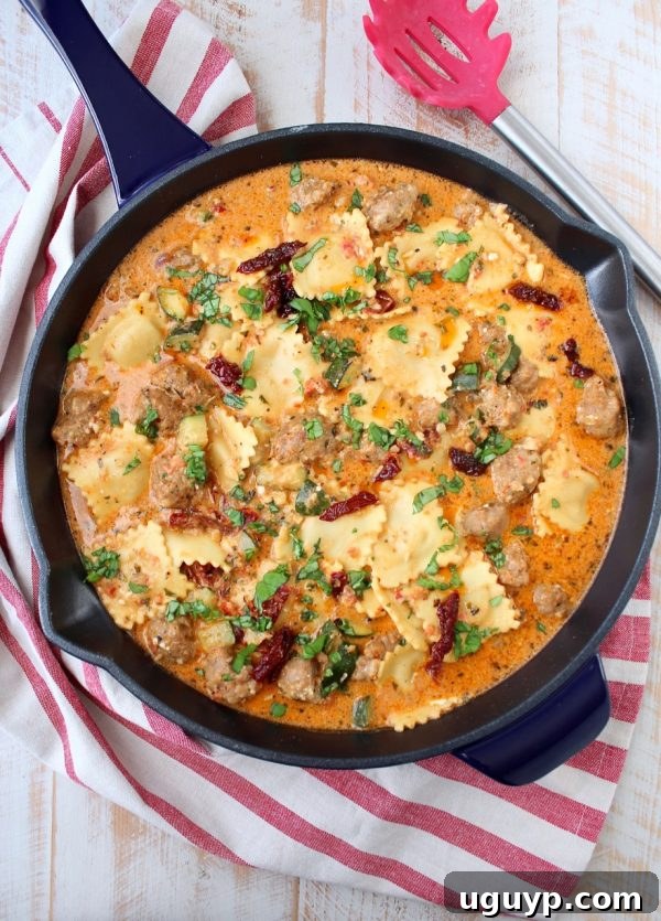 Large skillet filled with bubbling One Pot Ravioli, featuring a creamy pesto sauce, browned Italian sausage, and tender cheese ravioli.