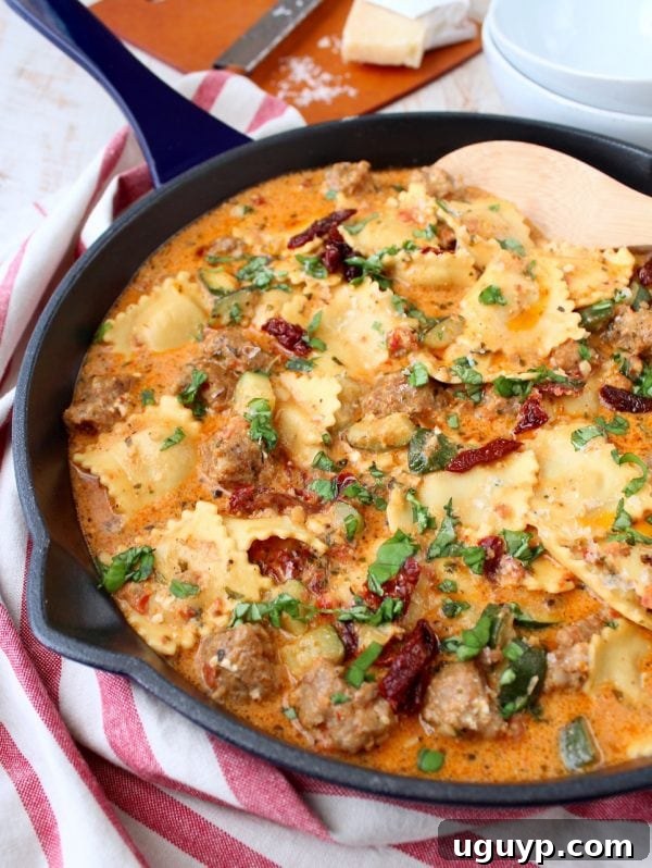 A close-up of a serving spoon lifting creamy pesto ravioli and sausage from a large pan.