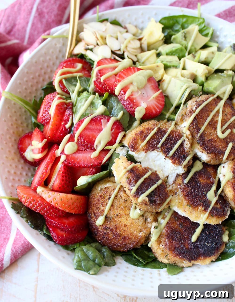 A vibrant Spring salad featuring crispy goat cheese, creamy avocado slices, and fresh strawberries over a bed of spinach and arugula, drizzled with avocado vinaigrette.