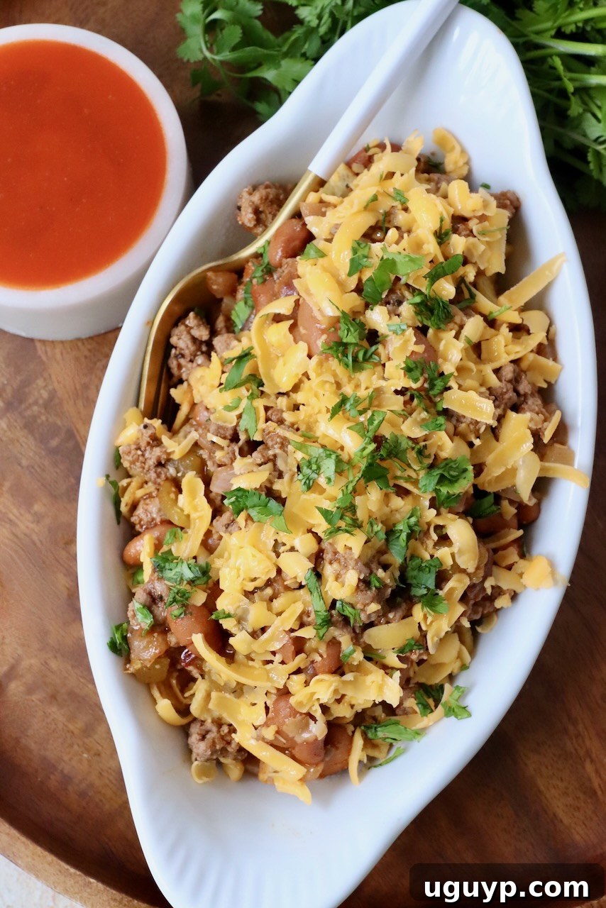 A close-up shot of Buffalo Frito Chili Pie served in a small white dish, with a fork dug in, showcasing the layers of crispy Fritos, rich chili, and melted cheddar cheese.
