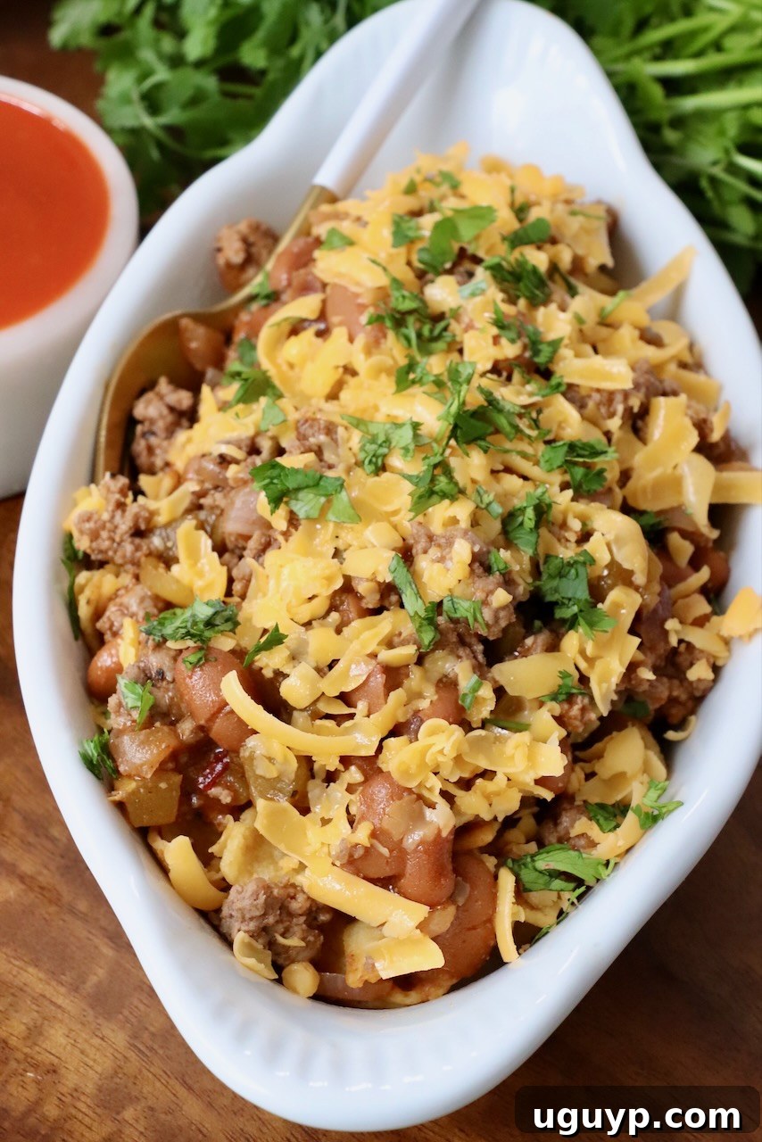 A white dish of Buffalo Frito Chili Pie with a fork, emphasizing its readiness to be enjoyed. The rich chili, crispy Fritos, and melted cheese are prominent.