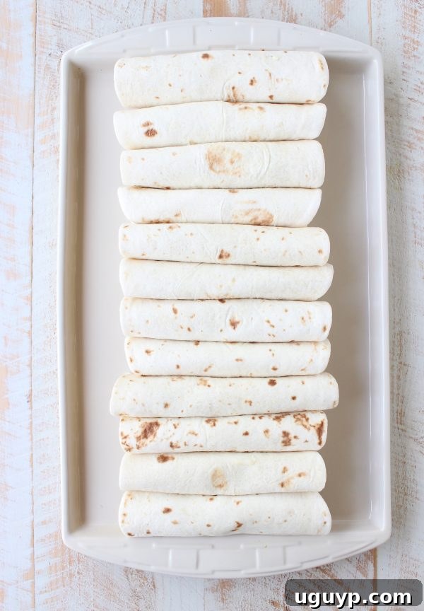 A tightly rolled Breakfast Taquito placed seam-side down on a baking sheet, ready for more taquitos.
