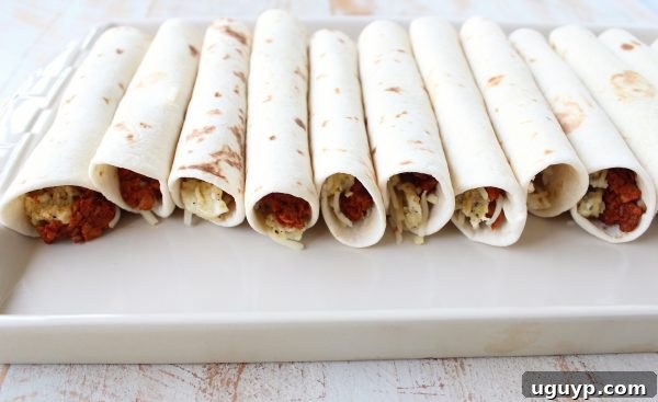 Multiple Breakfast Taquitos arranged neatly, seam-side down, on a baking sheet.