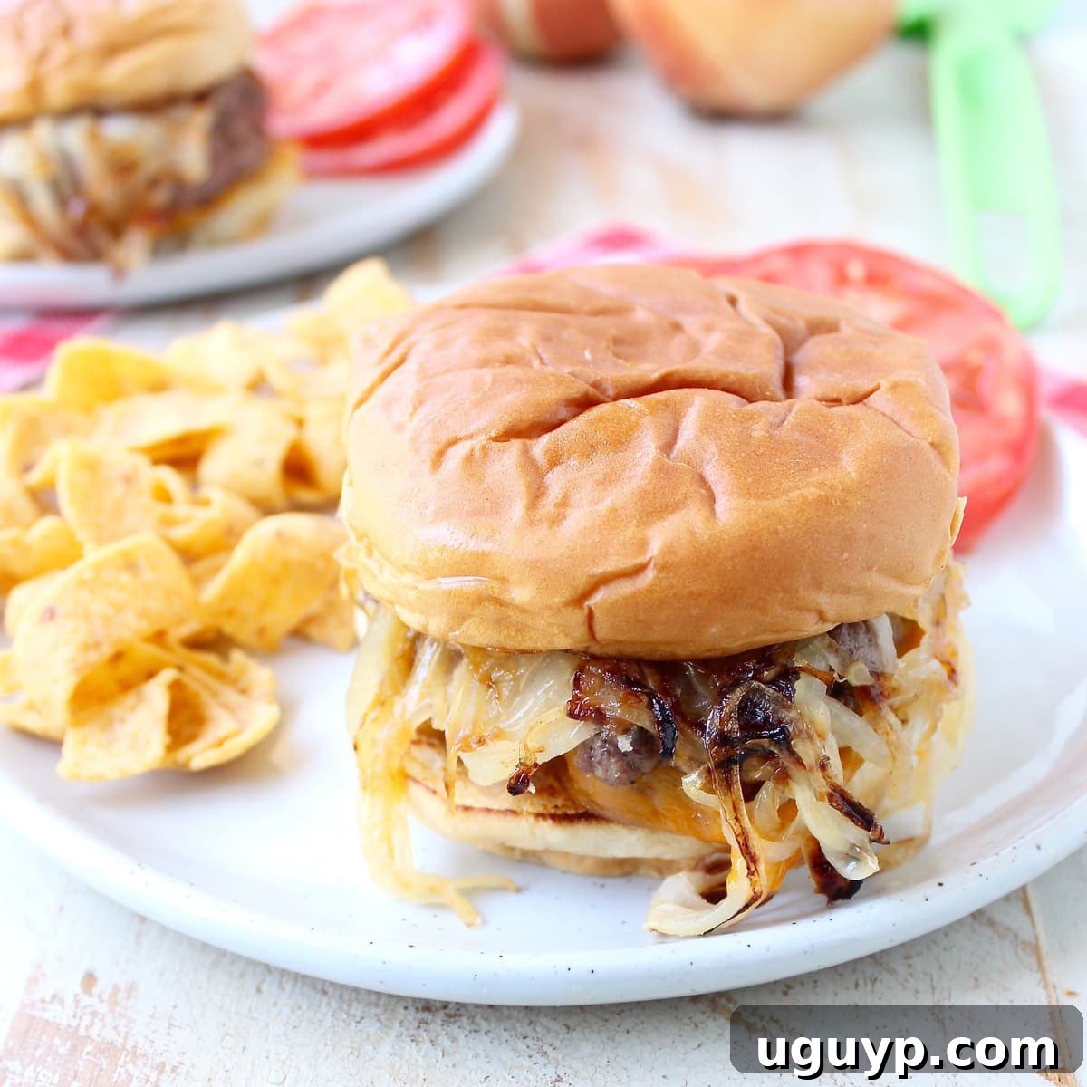 A delicious Oklahoma Fried Onion Burger served on a plate with Fritos chips and sliced tomatoes, showcasing its rich, savory appeal.