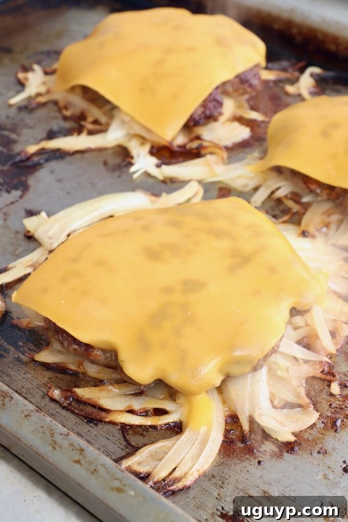 Cheese melting beautifully over the fried onion burgers on the griddle, signaling they are almost ready.