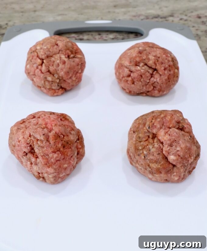 Four perfectly portioned balls of seasoned ground beef resting on a cutting board.