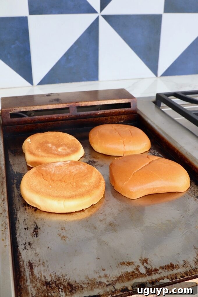 Hamburger buns toasting face-down on a hot griddle, achieving a perfect golden crisp.