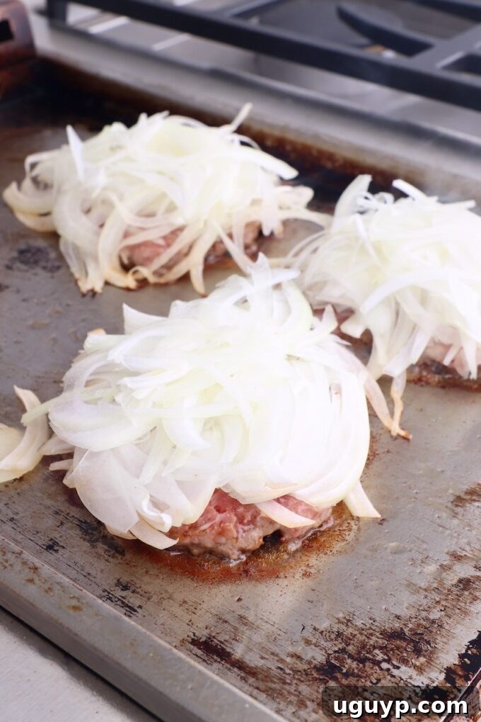 Thinly sliced onions generously layered on top of the sizzling smashed burger patties.