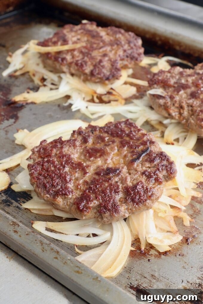 Burger patties flipped, with the grilled onions now caramelized beneath them on the hot griddle.