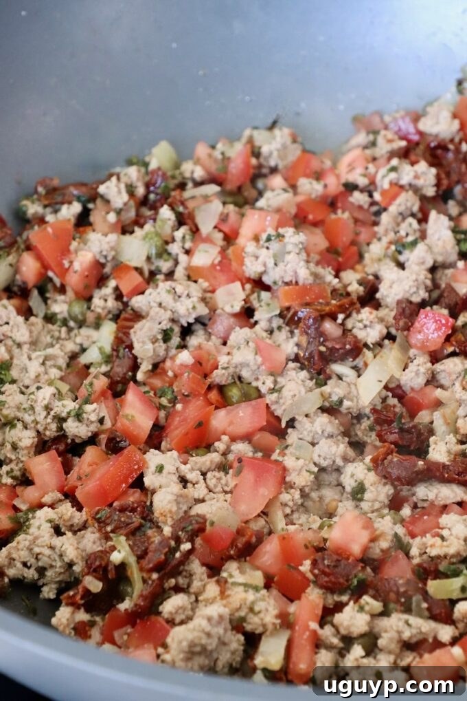 Ground turkey mixed with diced tomatoes and Mediterranean spices simmering in a pan, releasing rich aromas.