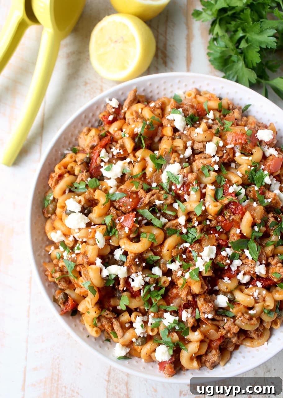 A close-up of the prepared one pot Greek pasta recipe in a white bowl, garnished with fresh chopped parsley and crumbled feta cheese, showcasing its vibrant colors and inviting texture.