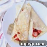 Crepes rolled up on plate filled with nutella and sliced strawberries