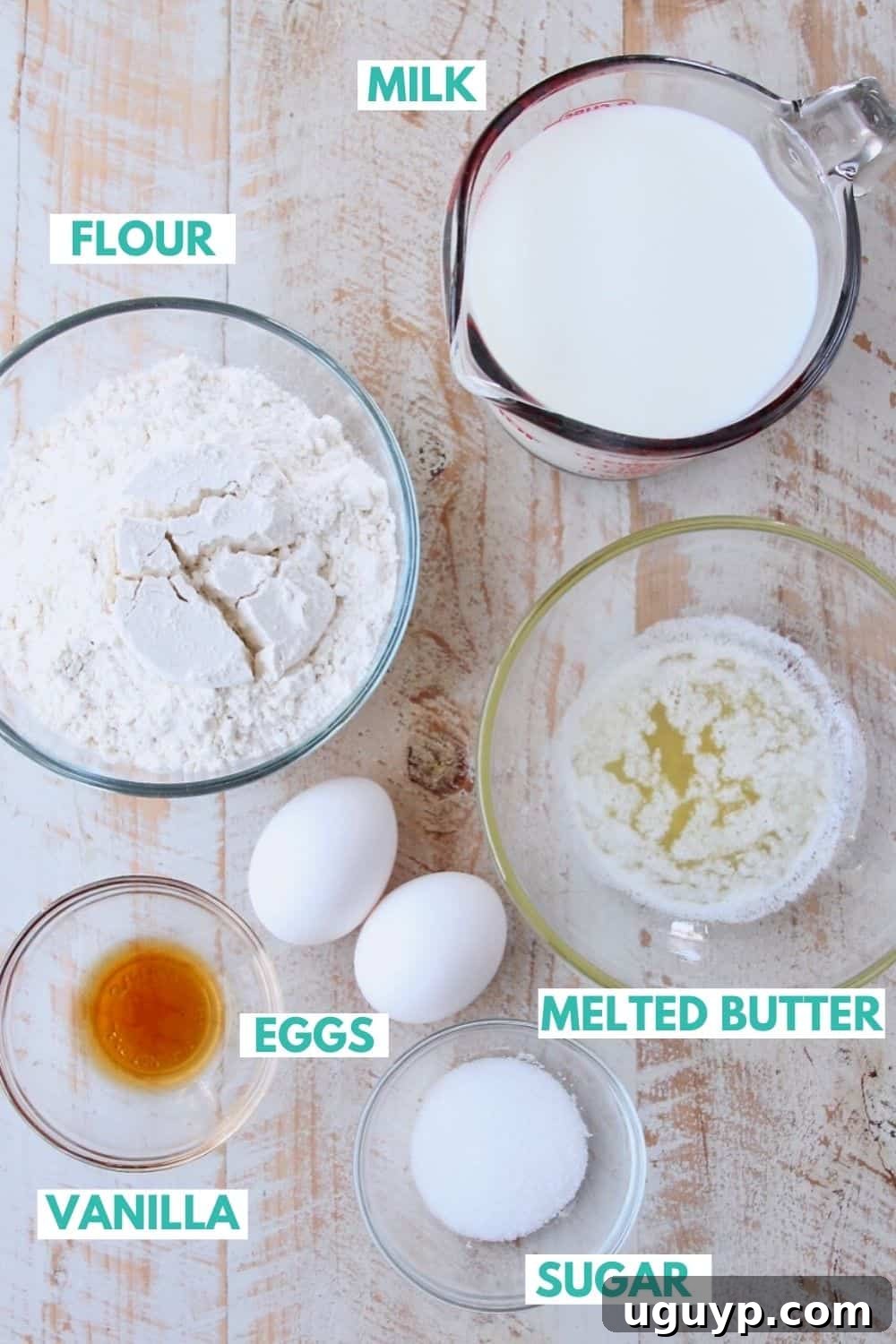 Fresh ingredients laid out on a white wooden board, ready for making homemade crepes: flour, milk, eggs, vanilla, and butter.
