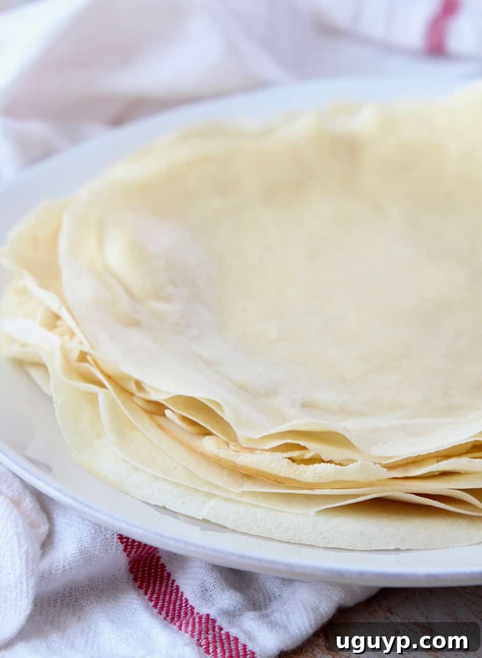 A stack of perfectly cooked golden-brown crepes resting on a plate, showcasing their delicate texture and readiness for fillings.