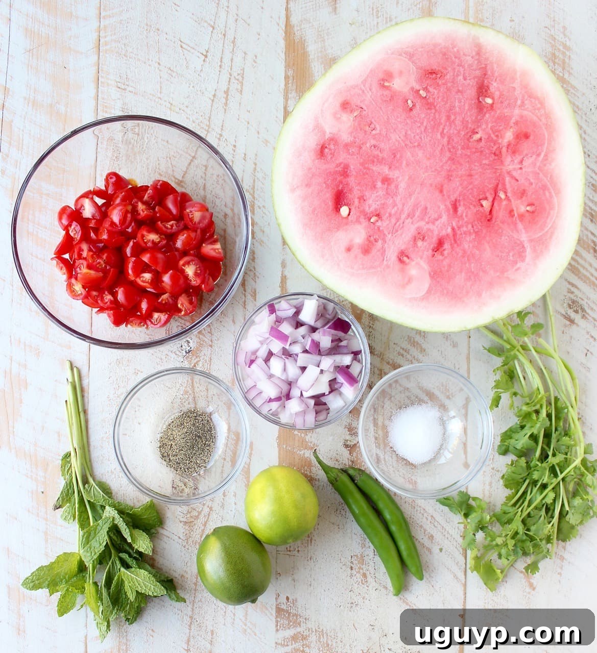 A selection of fresh watermelon salsa ingredients artfully arranged on a white wooden board, ready for preparation.