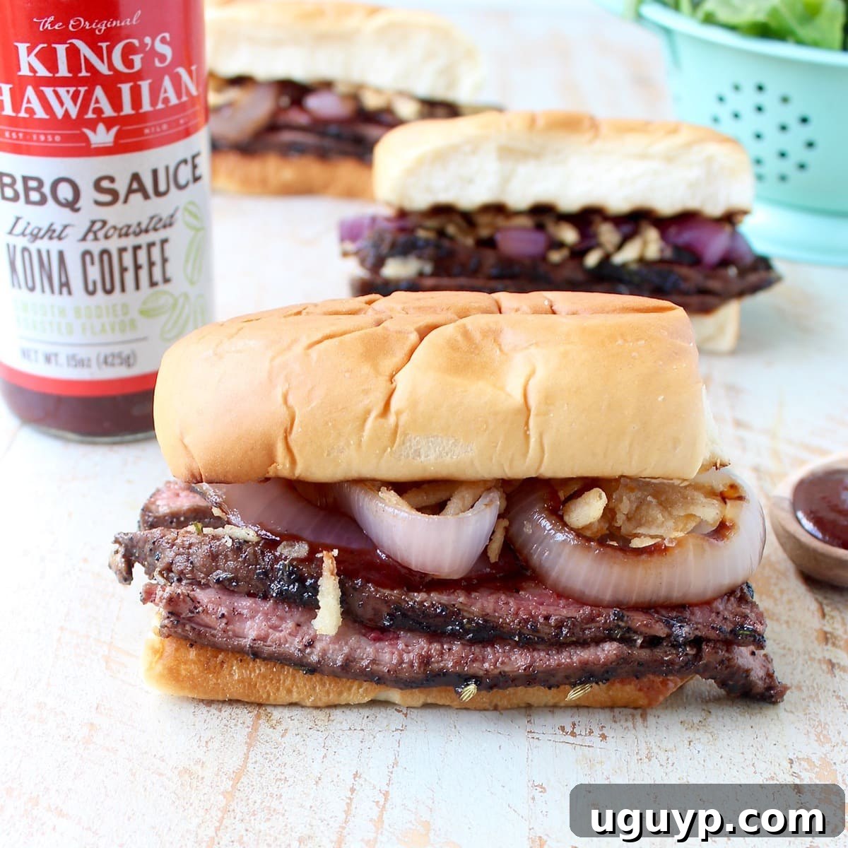steak sandwiches on white wood board with bottle of bbq sauce in the background