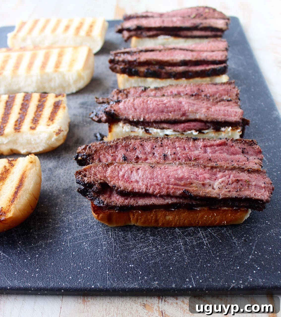 sliced, grilled steak on top of rolls on cutting board
