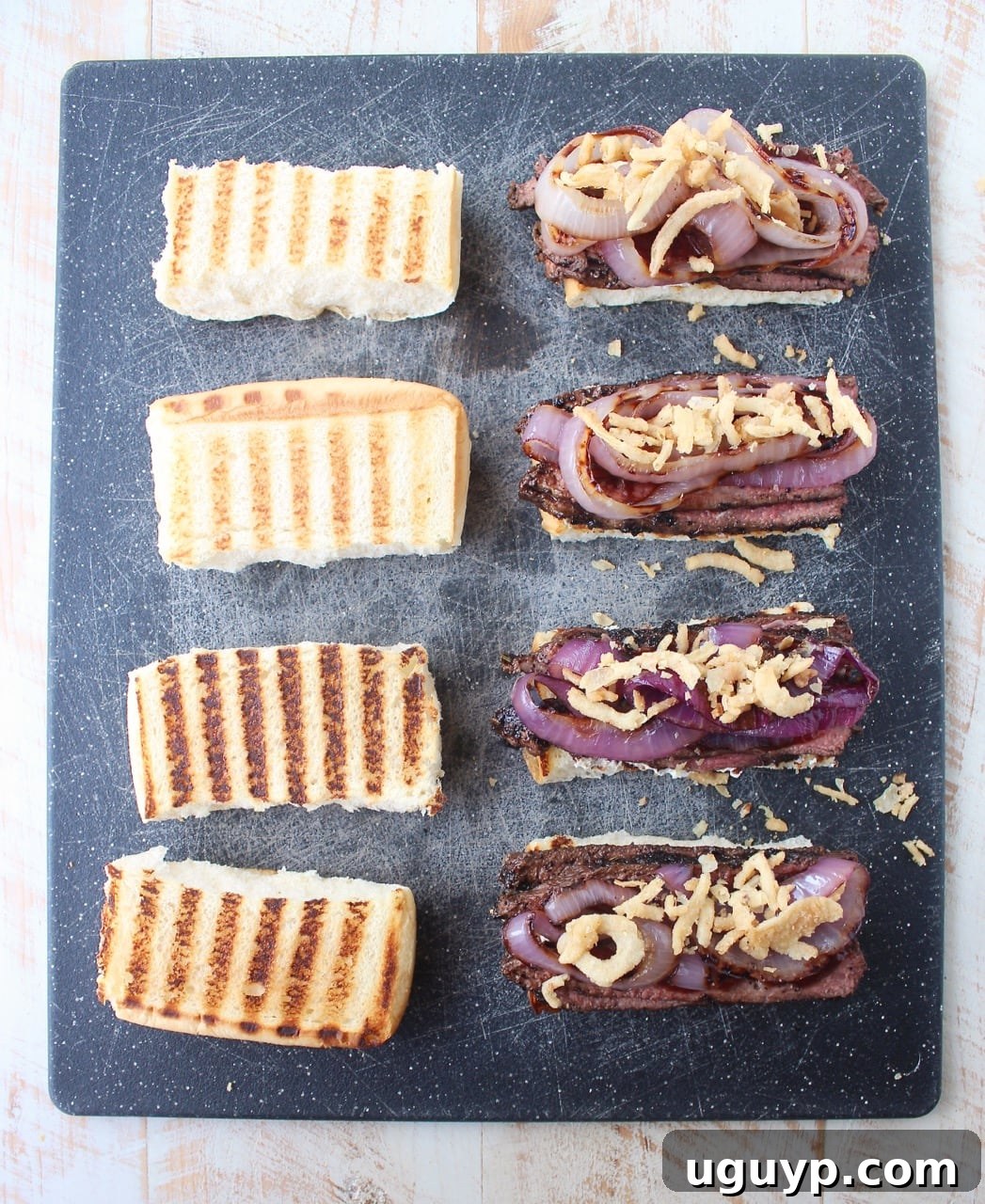 steak sandwiches on cutting board topped with grilled onions and crispy fried onions