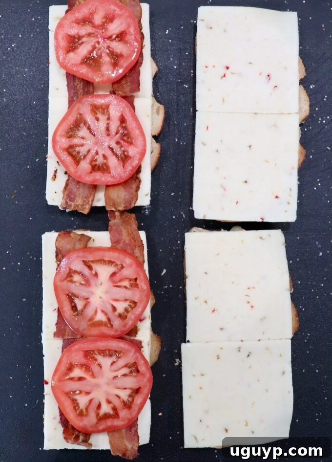bread topped with slices of pepper jack cheese, bacon and sliced tomatoes on cutting board