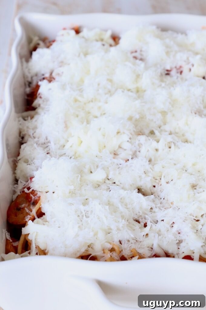 Uncooked spaghetti casserole topped generously with shredded mozzarella and parmesan cheese.