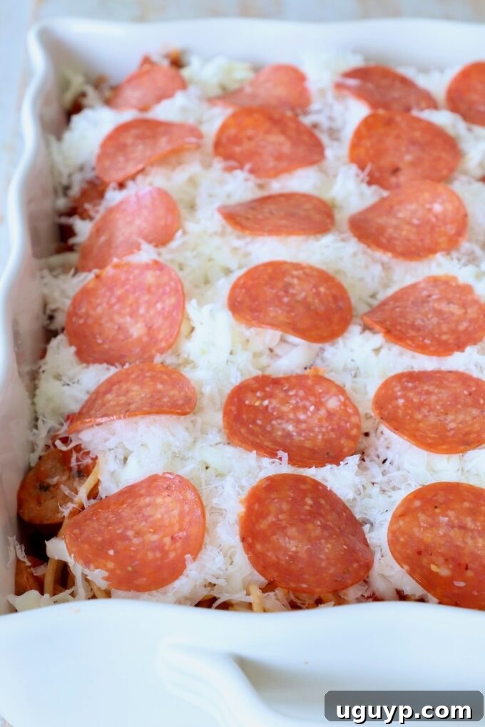 The spaghetti casserole, now topped with shredded cheese and an even layer of pepperoni slices, ready for the oven.