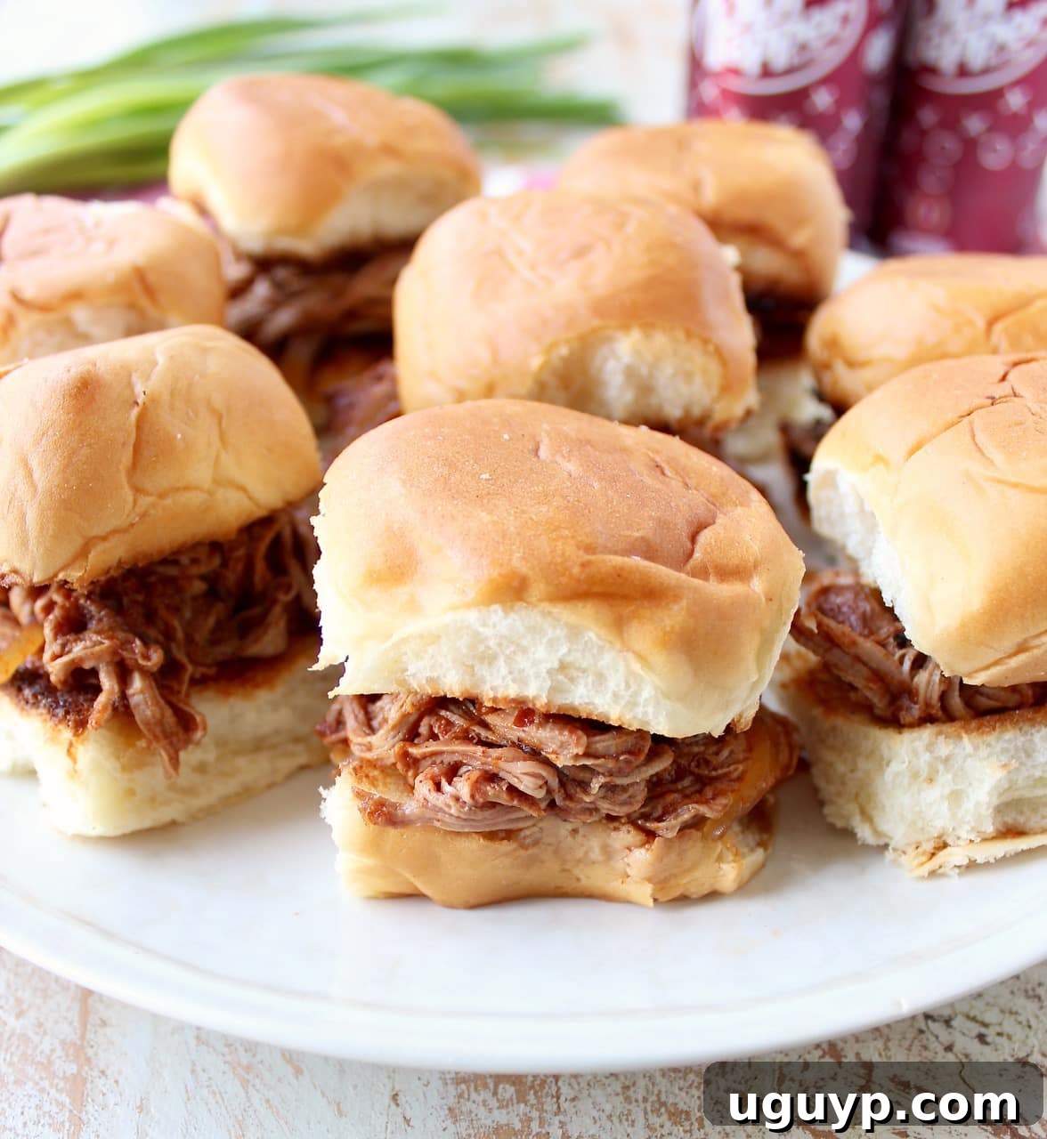 Hawaiian rolls filled with shredded Dr Pepper pulled pork, garnished and ready to serve on a white plate.