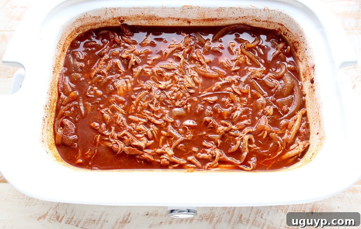 Shredded Dr Pepper pulled pork soaking in its flavorful sauce within the slow cooker.