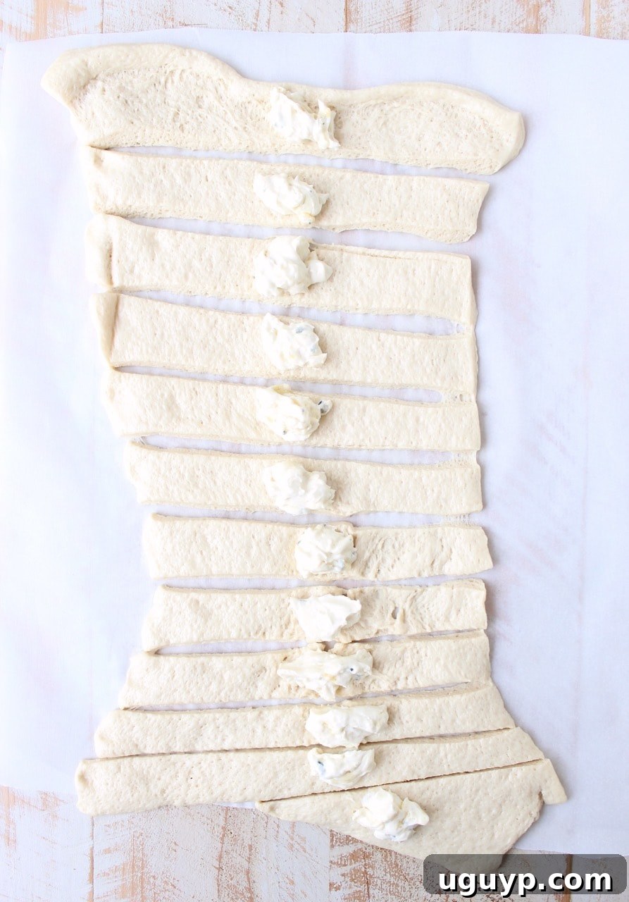 Pizza dough strips being filled with a cream cheese and blue cheese mixture before being tied into knots.